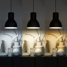 three white vases and two black ones on a shelf with lights in the background