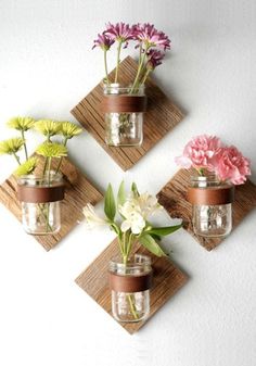 three mason jars with flowers are hanging on the wall