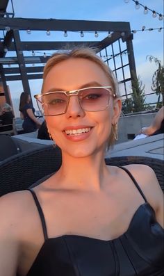 a woman wearing glasses sitting in a chair at an outdoor event and smiling for the camera