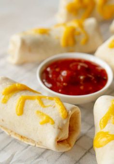 two burritos with cheese and ketchup are on the table next to some condiments