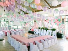 a room filled with lots of tables covered in white and pink tablecloths next to hanging decorations