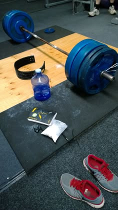 a pair of shoes sitting on the ground next to a barbell and water bottle