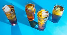 four glasses filled with different types of drinks on a blue table top next to each other