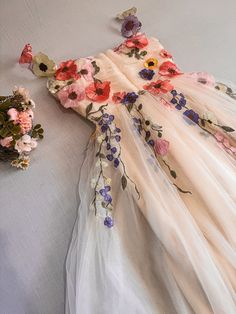 a white dress with flowers on it laying next to a flower pot