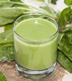 a glass filled with green liquid sitting on top of a table next to some leaves