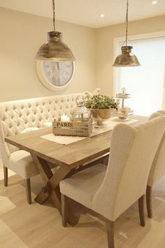 the dining room table is set with white chairs and upholstered banquet bench, along with two pendant lights