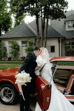 a bride and groom kissing in front of a red car