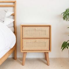 a nightstand with two drawers next to a bed and a plant in a pot on the floor