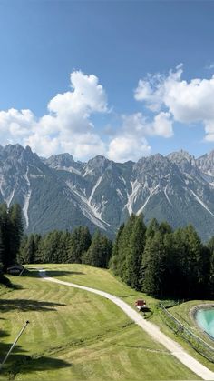 the mountains are covered in snow and green grass, with a path leading to a pond