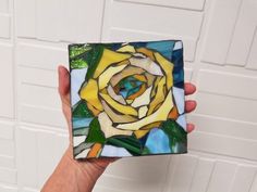 a hand holding up a small stained glass box with a yellow rose on it's side