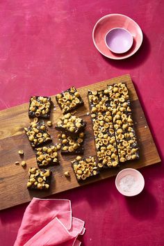 a wooden cutting board topped with pieces of food next to a pink napkin and cup