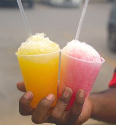 two people holding up drinks with straws in their hands on a street side walk