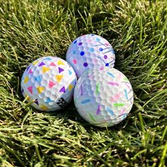 three golf balls sitting in the grass with colored sprinkles on each one