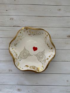 a white and gold plate with two bulls on it's side, holding a red heart