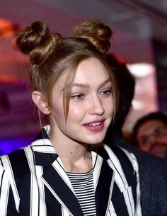 a woman with a messy topknot and striped shirt looks at the camera while standing in front of people