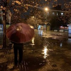 a person with an umbrella walking in the rain on a city street at night time