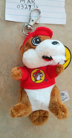 a brown and white stuffed animal with a red shirt on it's chest is attached to a keychain