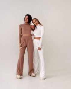 two women standing next to each other in white and brown outfits, both wearing matching pants