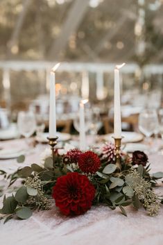 a table topped with candles and flowers on top of a white table cloth covered in greenery