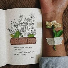 an open book with flowers on it and a hand holding a flower in front of it