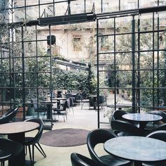 an indoor cafe with tables, chairs and plants on the wall behind glass doors that open up to outdoor seating