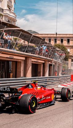 two red race cars driving down the street in front of some buildings and people watching