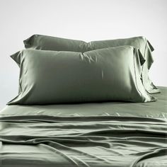 two pillows on top of a bed with green sheets and pillow cases in front of them