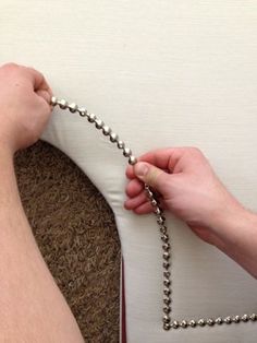 two hands holding onto a ball chain that is attached to a pillow on the floor