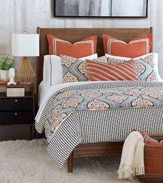 a bed with an orange and white comforter on top of it next to a night stand