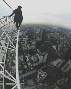 a man standing on the edge of a tall building while flying through the air over a city