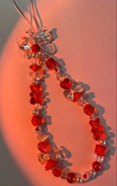 a necklace with red and white beads hanging from it's side on a pink surface