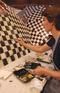 a woman is painting on a checkered wall with black and white tiles in the background