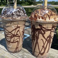 two iced drinks sitting on top of a wooden table covered in chocolate and whipped cream