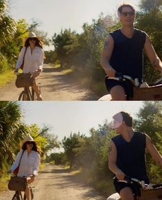 two people riding bikes down a dirt road with trees in the background and one person wearing a hat