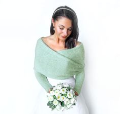 a woman in a white dress holding a bouquet of flowers and wearing a green sweater