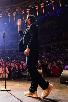 a man standing on top of a stage in front of a microphone and people watching