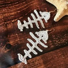 three white crocheted fish ornaments sitting on top of a wooden table next to an orange starfish