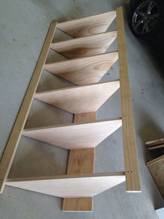 a wooden shelf sitting on top of a floor next to a black car in a garage