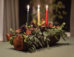 candles are lit on a table with greenery and pine cones