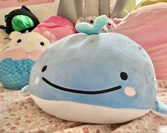 a blue whale stuffed animal sitting on top of a bed next to pillows and toys