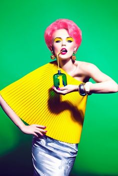 a woman with bright pink hair holding a green bottle in her hand and wearing yellow