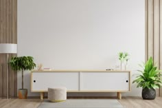 a living room with white walls and wooden flooring, potted plants on the sideboard