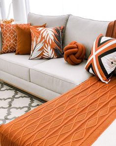 an orange and white couch with pillows on it in a living room next to a window