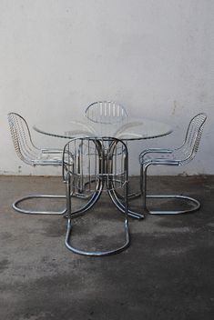 a glass table with four chairs sitting on top of it next to a white wall