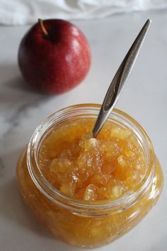 an apple is sitting next to a jar of fruit jam with a spoon in it