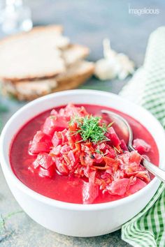 a white bowl filled with red soup and garnished with fresh herbs on top