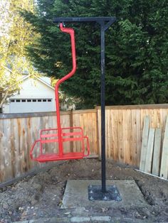 a red metal object sitting in the middle of a dirt area next to a fence