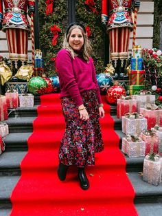 a woman standing on the red carpeted stairs in front of christmas decorations and presents