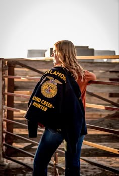 a woman standing in front of a fence wearing a jacket that says canyon creek hunter