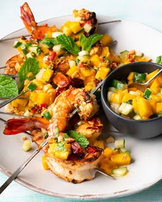 a white plate topped with shrimp and mango salad next to a bowl of salsa dressing